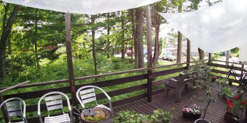 a porch with chairs and a fence with trees at Bellscabin Guesthouse in Karuizawa