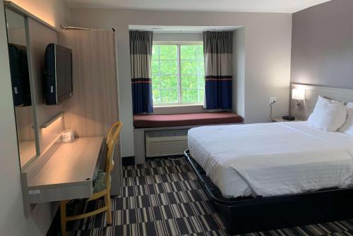 ein Hotelzimmer mit einem Bett, einem Schreibtisch und einem Fenster in der Unterkunft Microtel Inn by Wyndham Charlotte Airport in Charlotte
