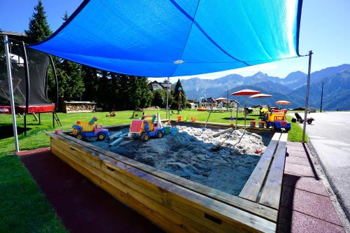 a sandbox with toys in the sand under a blue umbrella at Apart-Hotel Dreisonnenhof in Fiss
