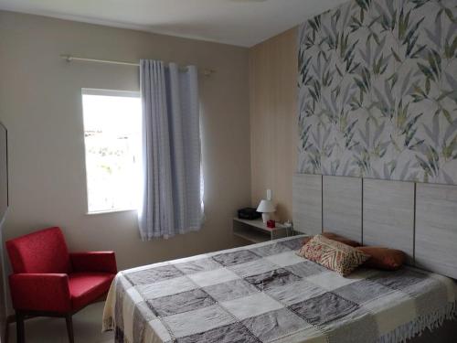 a bedroom with a bed and a red chair and a window at Residencial Verano 105C in Guarajuba