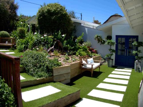 a garden with a bench and a blue door at Long Story Guest House in Plettenberg Bay