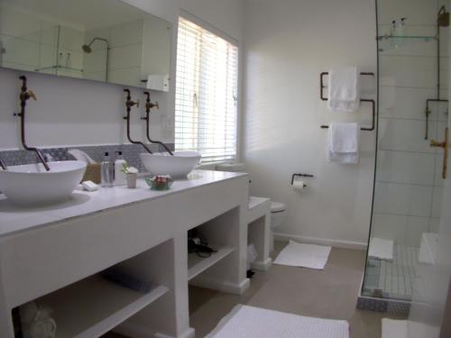a white bathroom with two sinks and a shower at Long Story Guest House in Plettenberg Bay