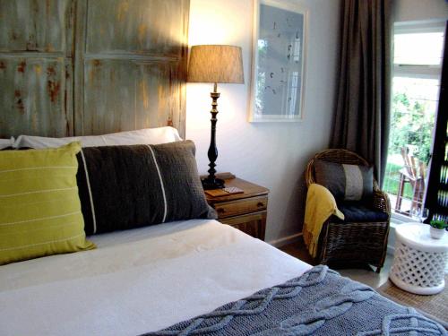 a bedroom with a bed and a chair and a lamp at Long Story Guest House in Plettenberg Bay