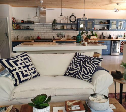 a living room with a white couch in front of a kitchen at Long Story Guest House in Plettenberg Bay