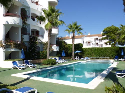 a swimming pool in front of a building with palm trees at Sagitario Vista Playa I Apartamentos in Cala Blanca