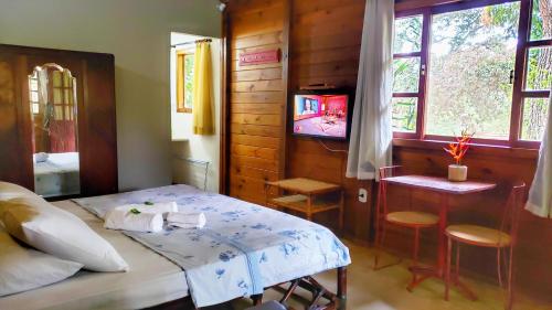 a bedroom with a bed and a table and a tv at Pousada Camping Porto Grande in Meaípe