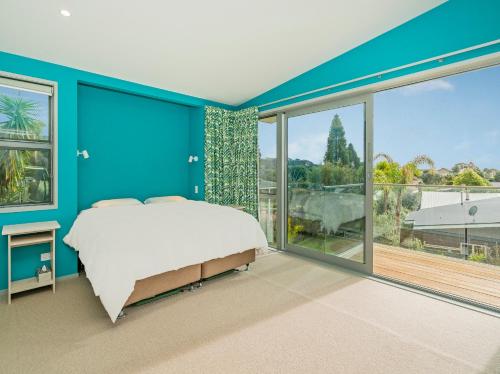 a blue bedroom with a bed and large windows at A Slice of Summer - Whangapoua Holiday Home in Whangapoua