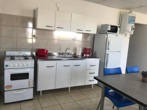 Una cocina con electrodomésticos blancos y una mesa con sillas. en Departamentos Alberdi 3, en San Rafael