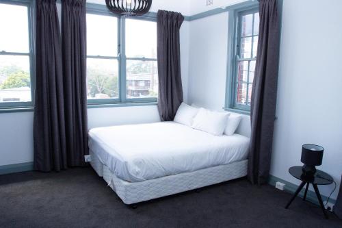 a bed in a room with two windows at Oasis on Beamish Hotel in Sydney