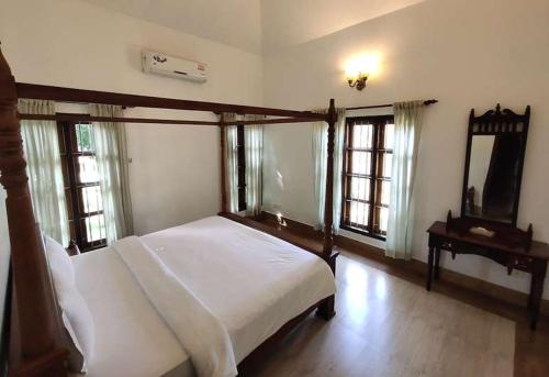 a bedroom with a bed and a mirror and windows at Rasa Gurukul in Kizhake Chālakudi