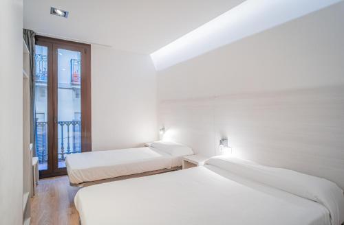 two beds in a white room with a window at Hostal Fina in Barcelona