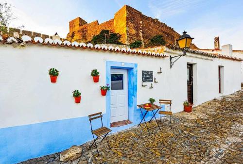 a white building with a blue door and chairs at Casa do Castelo - Zona Histórica in Mértola