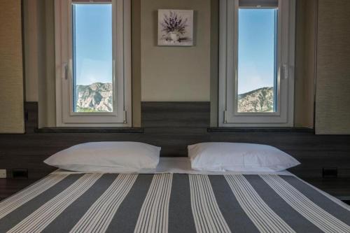 a bed with two pillows in a room with windows at Foresteria La Merlina in Borgo Adorno