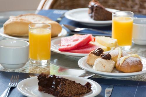 a table with plates of food and glasses of orange juice at Hotel Ilhas da Grécia in Guarujá