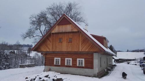 a small wooden house with a dog standing in the snow at Farma Hermína in Jilemnice