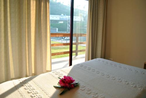 a book with a flower on top of a bed with a window at Alojamento das Caldas in Caldas de Aregos