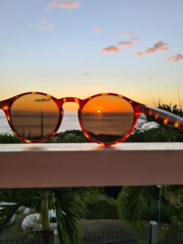 a pair of sunglasses sitting on a railing with a sunset at PARADIS AU SOLEIL, vue panoramique sur mer in Bouillante