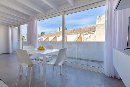 Una mesa y sillas blancas en una habitación con ventanas grandes. en Le Cupole Suites & Apartments en Trapani