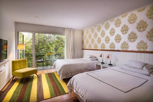 a bedroom with two beds and a yellow chair at Hotel Casa Zapallar in Zapallar