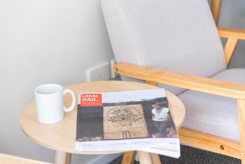 a table with a coffee cup and a magazine on it at Raglan Sunset Motel and Conference Venue in Raglan