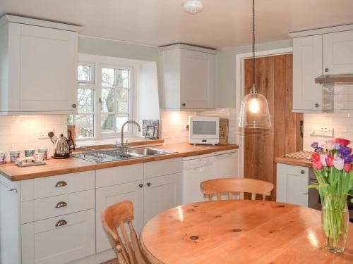 a kitchen with white cabinets and a wooden table at Derwent Cottage in Malton
