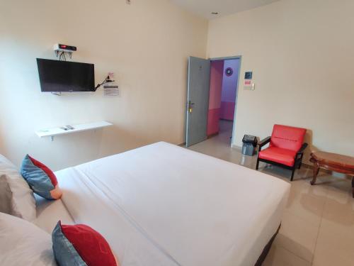 a bedroom with a white bed and a red chair at Ayuning Guest House Syariah Semarang Mitra RedDoorz in Semarang