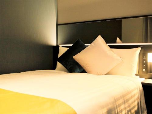 a bedroom with a white bed with black pillows at QuintessaHotel FukuokaTenjin Comic&Books in Fukuoka