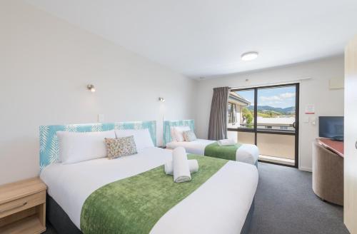 two beds in a hotel room with a balcony at Bella Vista Motel Nelson in Nelson