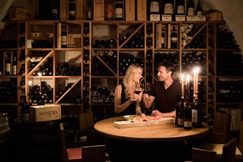 a man and woman sitting at a table with wine glasses at Lake Spa Hotel SEELEITEN in Caldaro