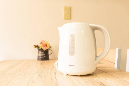 a white kettle sitting on a table with a vase of flowers at Airstar Hakata House in Fukuoka