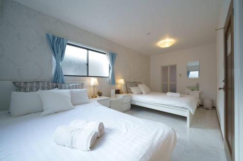 a white bedroom with two beds and a window at Airstar Hakata House in Fukuoka