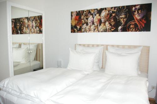 1 cama blanca con almohadas blancas y una pintura en la pared en The Suite Hotel Garden, en Frankfurt