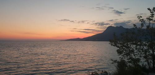 a sunset over a body of water with a mountain at Cozy apartments with seafront terraces in Omiš