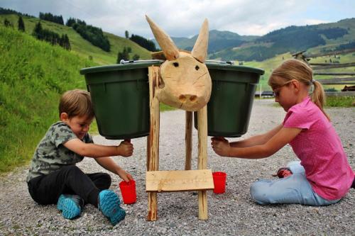 a boy and a girl playing with a toy goat with buckets at Bauernhof Hotel Oberschwarzach in Saalbach Hinterglemm