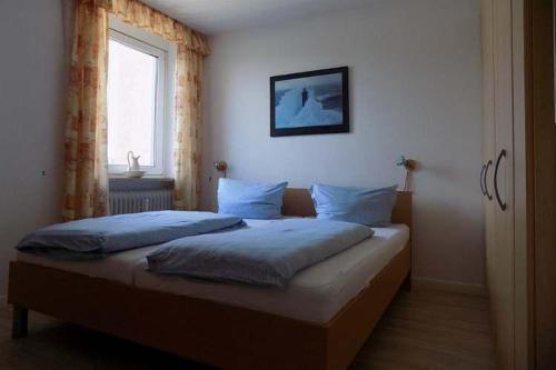 Un dormitorio con una cama con almohadas azules y una ventana en Haus Uthlande Uthlande Whg 5 Seepferdchen en Wyk auf Föhr