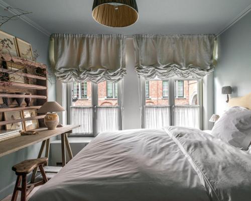 a bedroom with a bed and a desk and windows at Guesthouse Dijver - Serene Escape in the Heart of Historic Bruges in Bruges