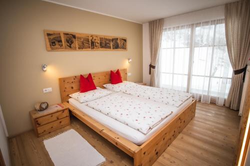 - une chambre avec un grand lit en bois et des oreillers rouges dans l'établissement Apartment CANUS - Krumas Living - Kronplatz, à San Lorenzo di Sebato