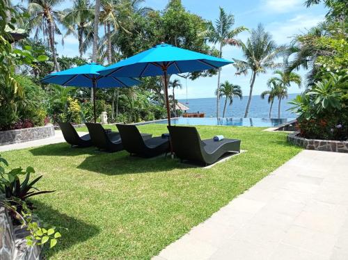 a row of chairs and umbrellas next to the ocean at Absolute Beachfront, Paradise, 3BR Villa with Private Pool on 1200m2 of Tropical Land in Tulamben