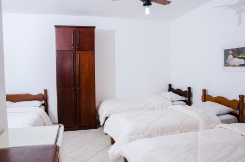 a room with four beds with white sheets and a wooden cabinet at Hotel Morada do Mar in Guarujá