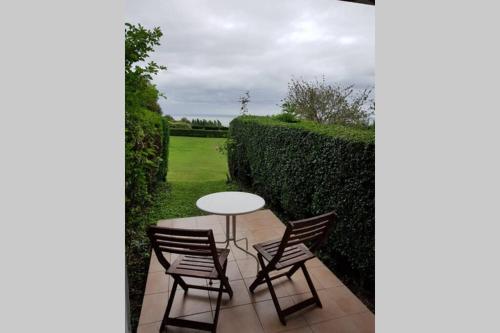 une terrasse avec une table, des chaises et une haie dans l'établissement Studio cosy et terrasse-jardin superbe vue mer, à Trouville-sur-Mer