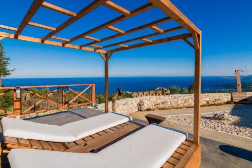 a wooden pergola with white chairs and the ocean at Nikolakos Villa in Agios Nikolaos