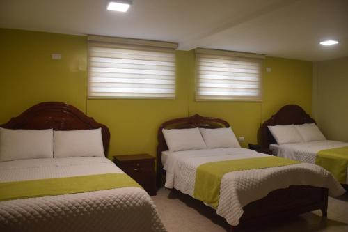 two beds in a room with green walls and windows at Hotel Cayapas Esmeraldas in Esmeraldas