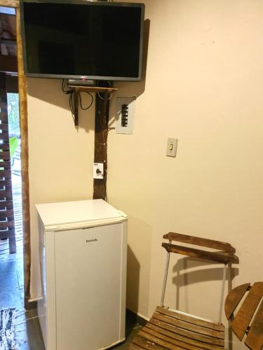 a flat screen tv on a wall with a small refrigerator at Chalés Catavento in Maresias