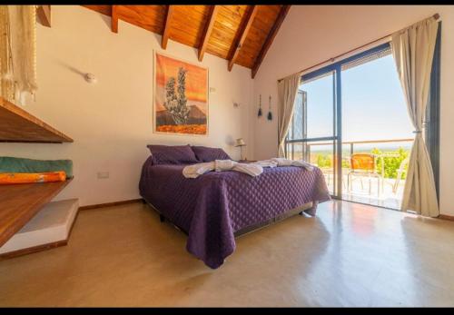 Un dormitorio con una cama morada y una gran ventana. en Villa Bautista, en Santa Rosa de Calamuchita