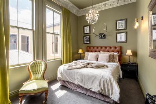 um quarto com uma cama, uma cadeira e um lustre em The Royal Hotel Featherston - Boutique Hotel em Featherston