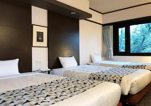 a hotel room with three beds and a window at Hotel Okus in Kumamoto