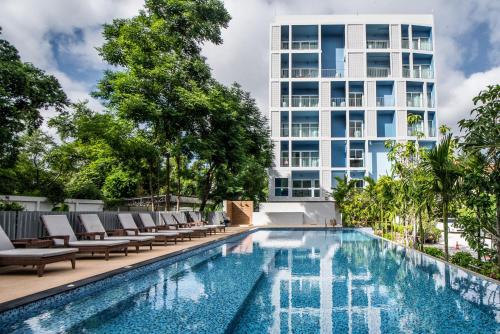 a swimming pool with lounge chairs and a tall building at DeeProm Pattaya Hotel in Pattaya Central
