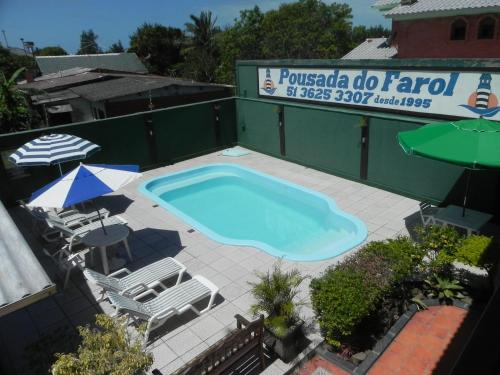 an empty swimming pool with chairs and an umbrella at Pousada Do Farol in Capão da Canoa