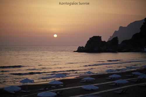 a beach with umbrellas and the ocean at sunset at Villa Caesar in Agios Ioannis
