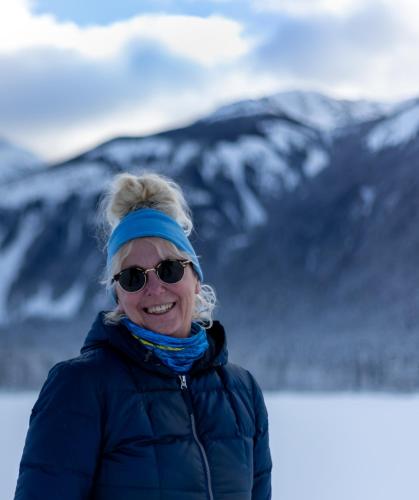 a woman wearing sunglasses and a blue jacket with mountains in the background at Rose Cottage Bed & Breakfast in Valemount